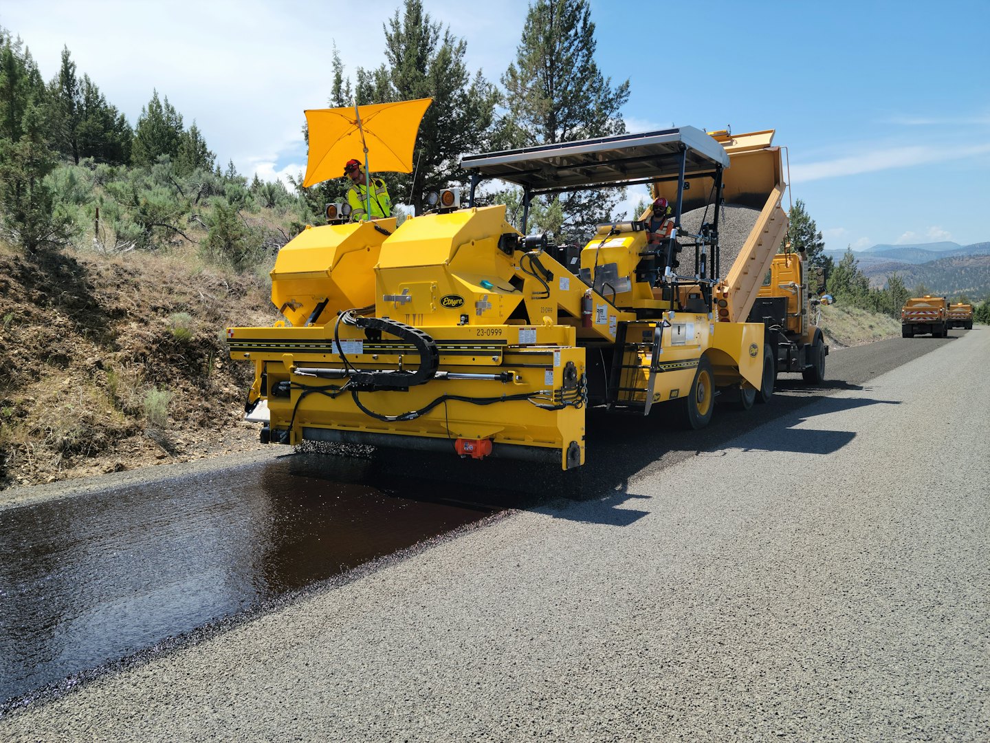 Construction workers use paving machines to lay asphalt on a road.