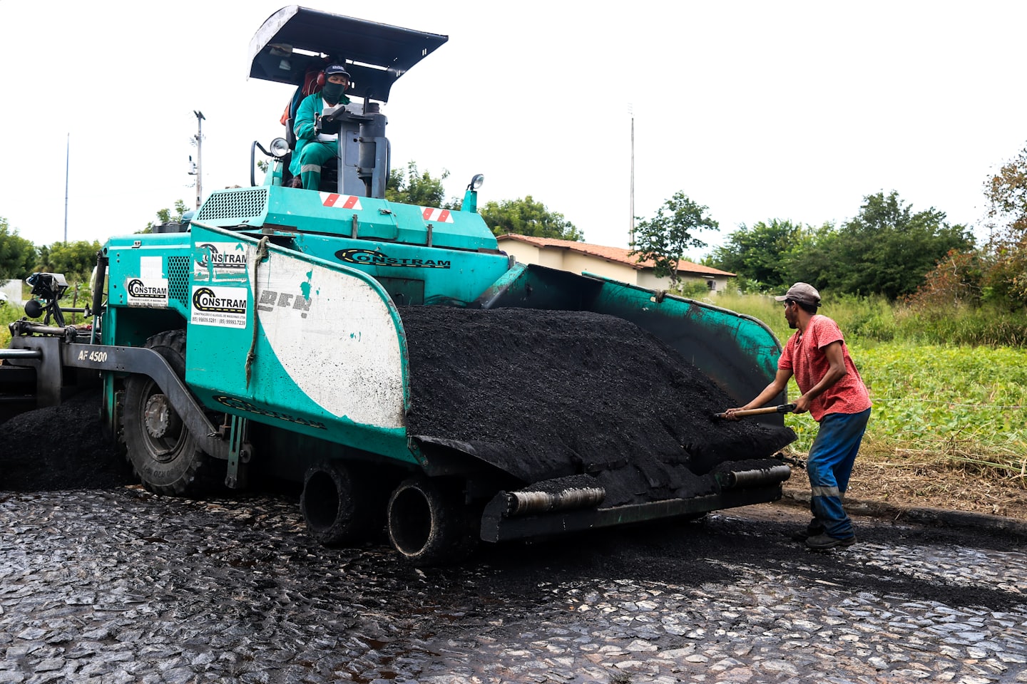 Construction workers pave a road with an asphalt paver.