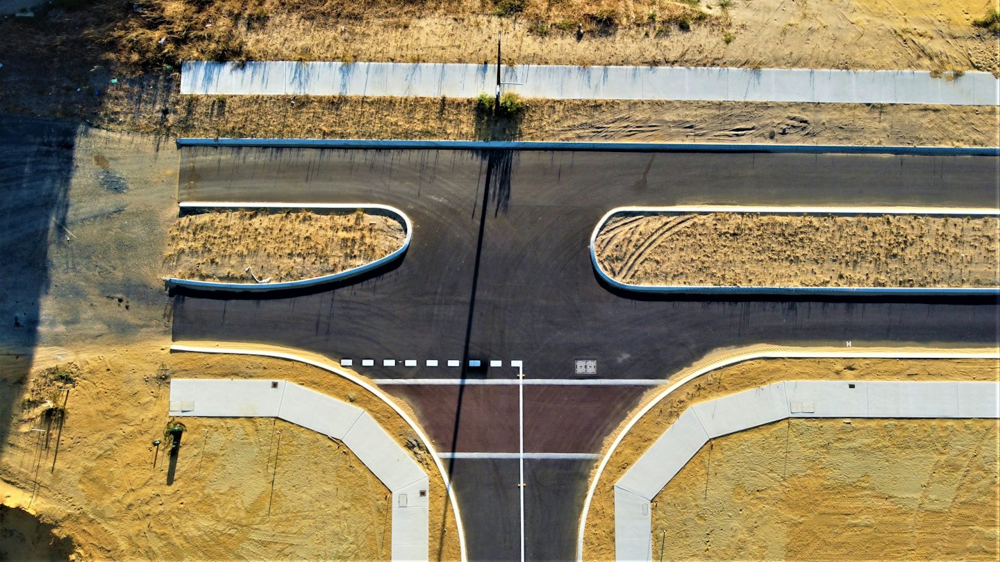 A new asphalt T-intersection sits surrounded by bare construction earth.