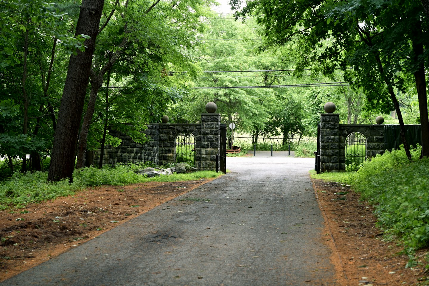 An asphalt path leads through an ornate stone gate.